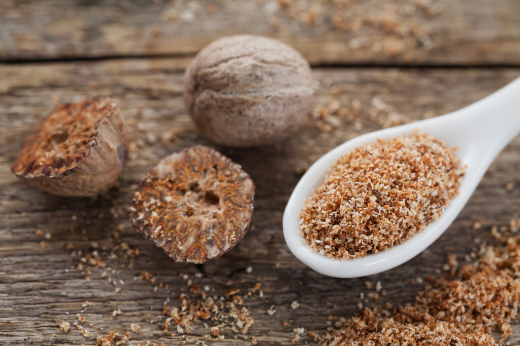 Nutmeg whole and grated on wooden background, selective focus